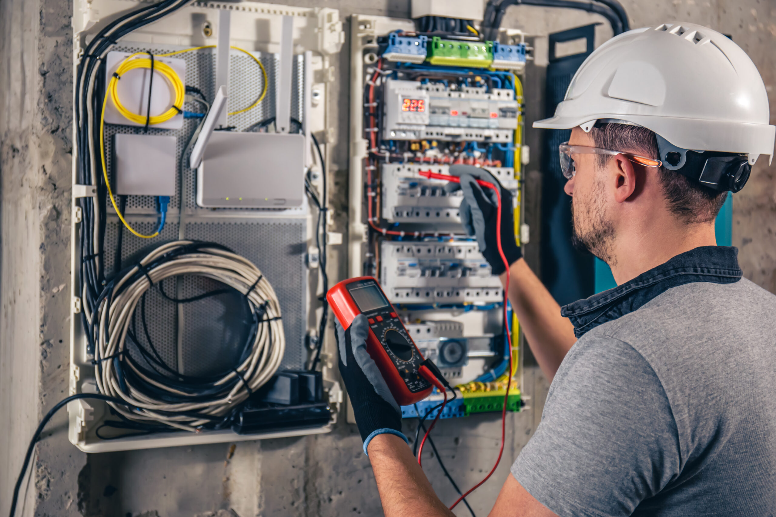 Man, an electrical technician working in a switchboard with fuses. Installation and connection of electrical equipment. Professional uses a tablet.